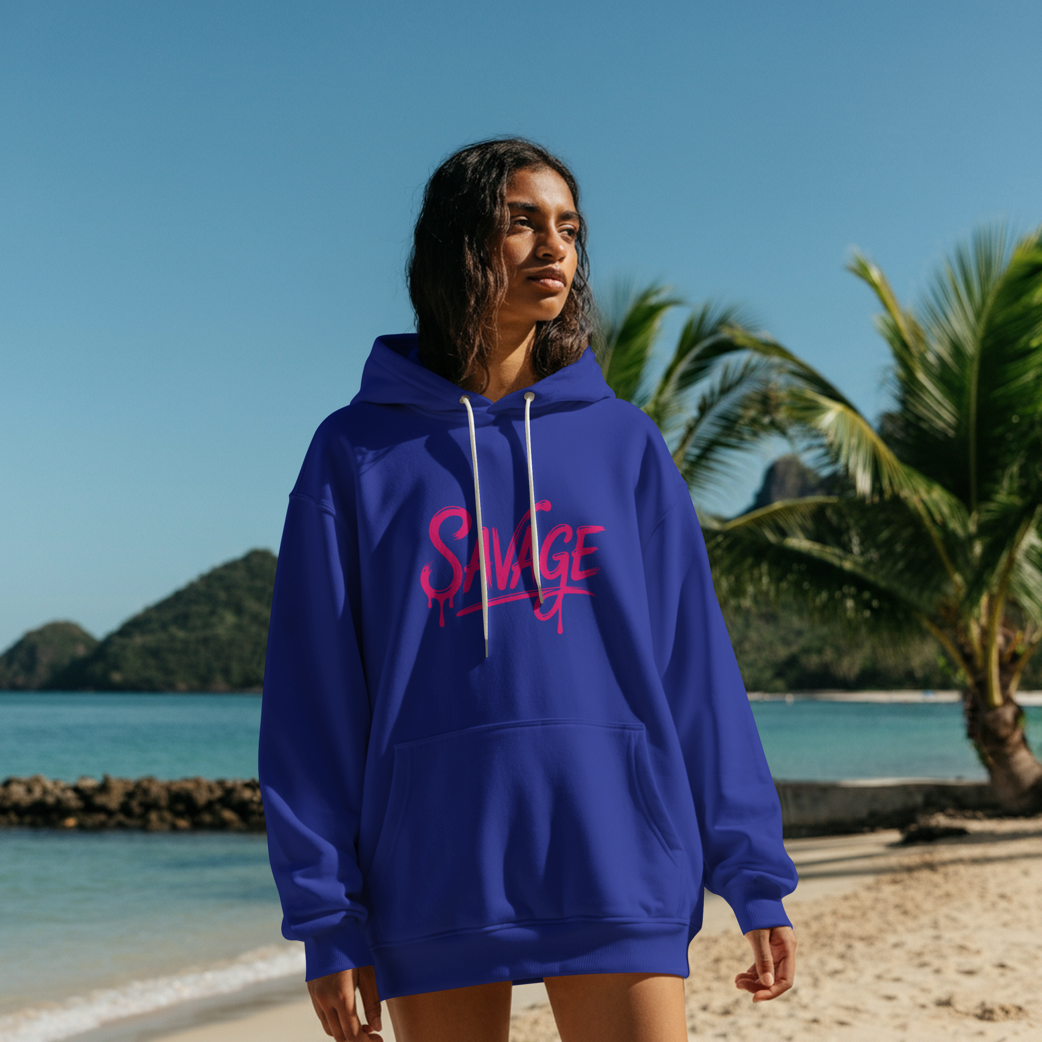 Woman wearing blue Savage Drip Hoodie with pink logo on a beach background
